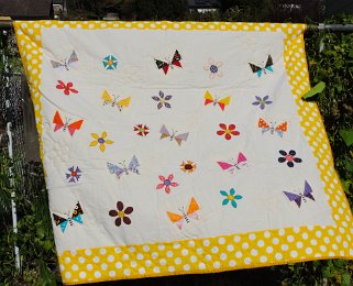 Schmetterlinge - auf dieser fröhlichen Kinderdecke tummeln sich unterschiedliche Schmetterlinge zwischen applizierten Blüten.  Maße: 153x139cm Preis: € 320.- 
